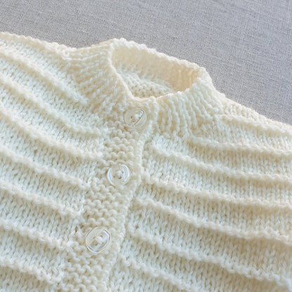Close-up of a light green knitted garment with button details on a gray background