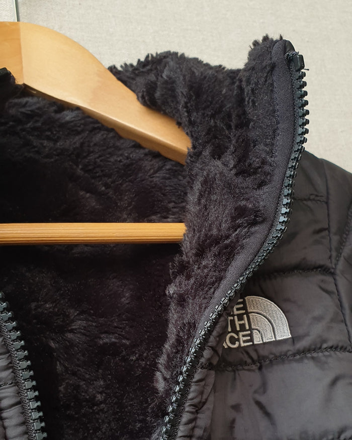 Close-up of a black puffer jacket with a wooden hanger on a light gray background